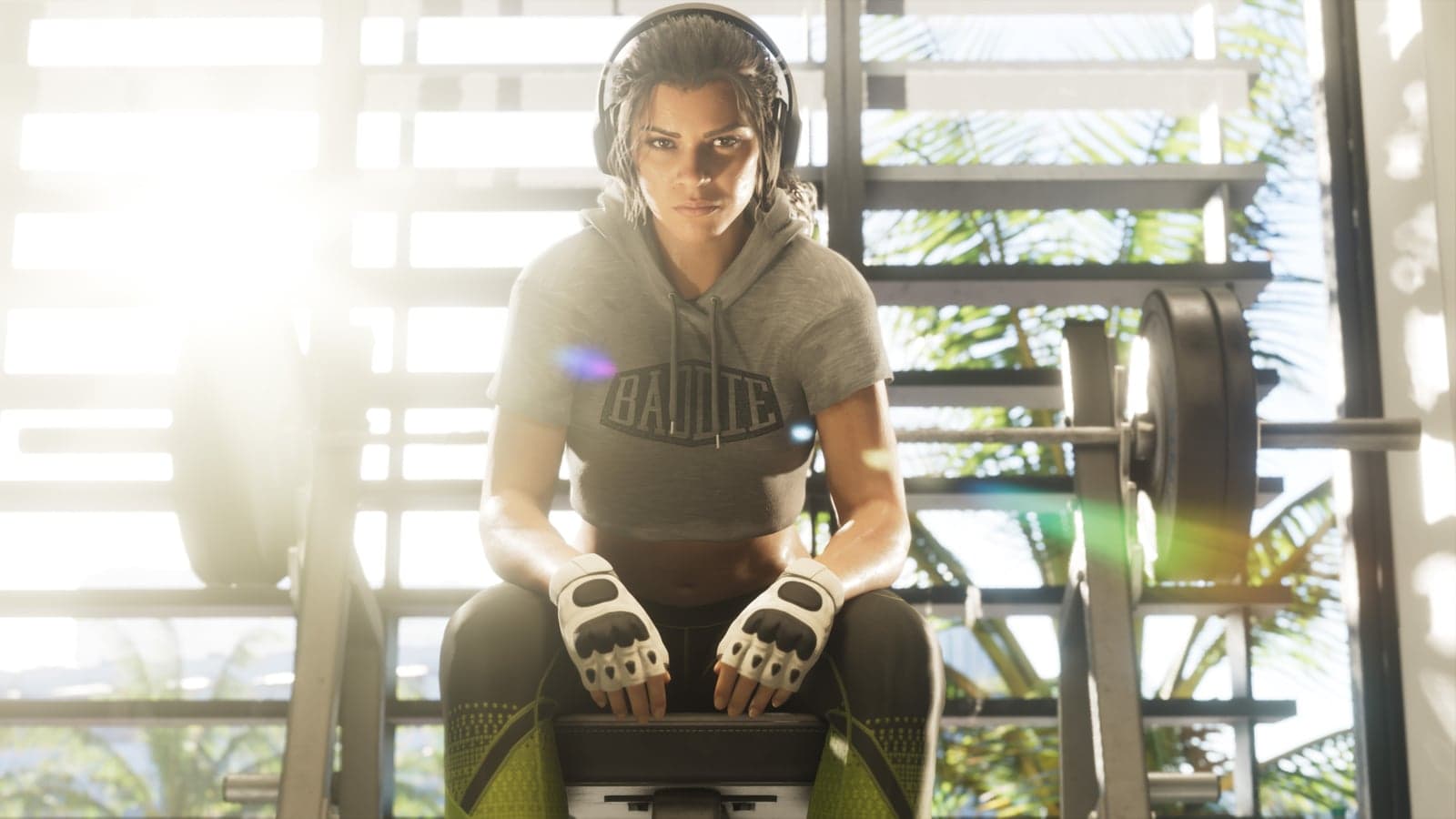 Lucia in a gray hoodie and training gloves sits on a gym bench