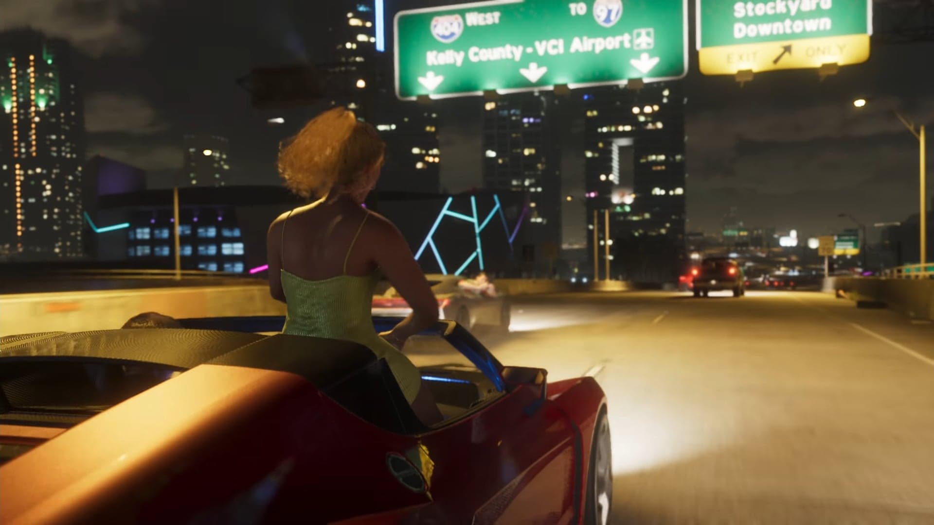 A girl on the back of a red convertible on a night highway under signs for VCI Airport and Stockyard Downtown