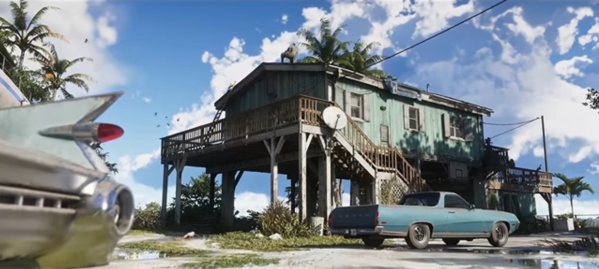 A house on stilts by the water, with an old finned car in the foreground and a pickup in the yard