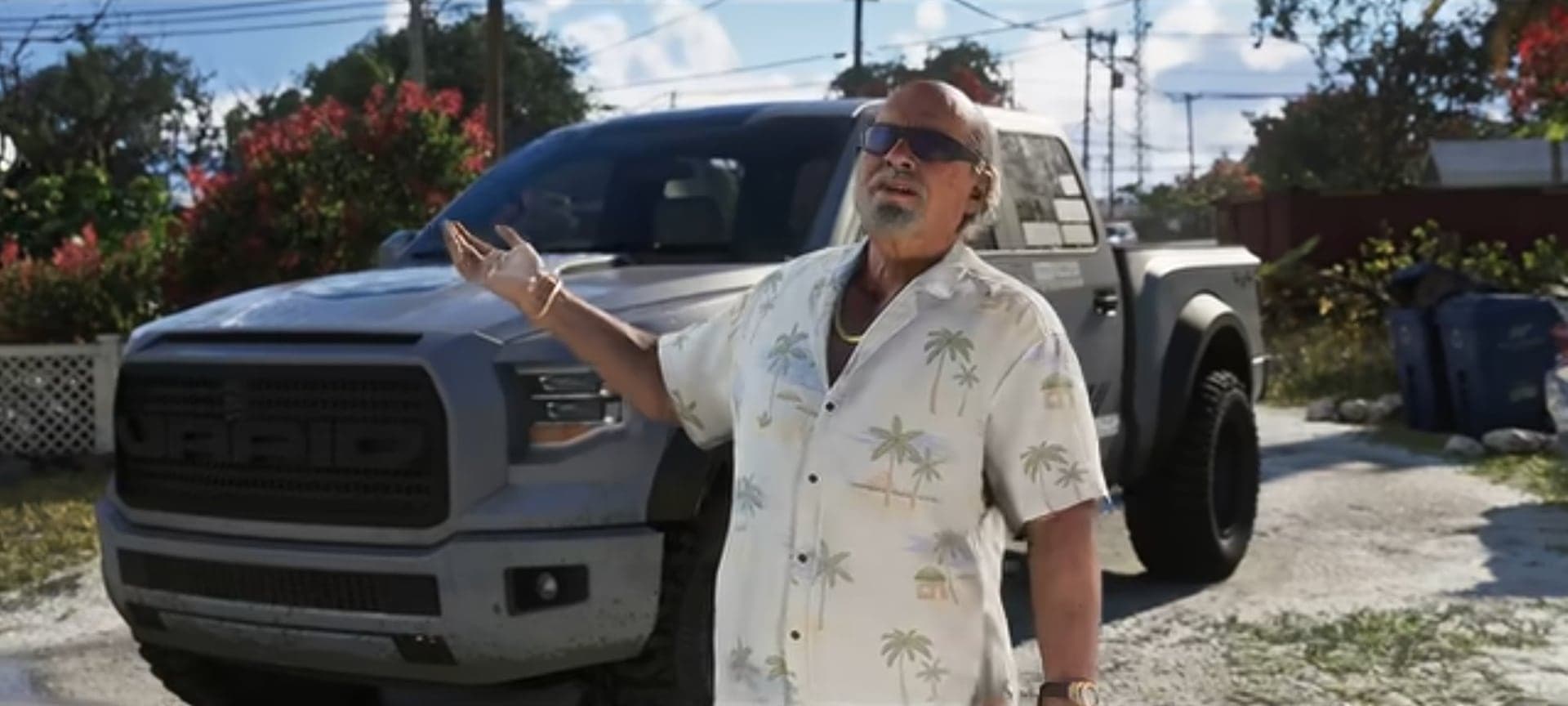 Brian in a Hawaiian shirt and sunglasses gesturing by a gray pickup