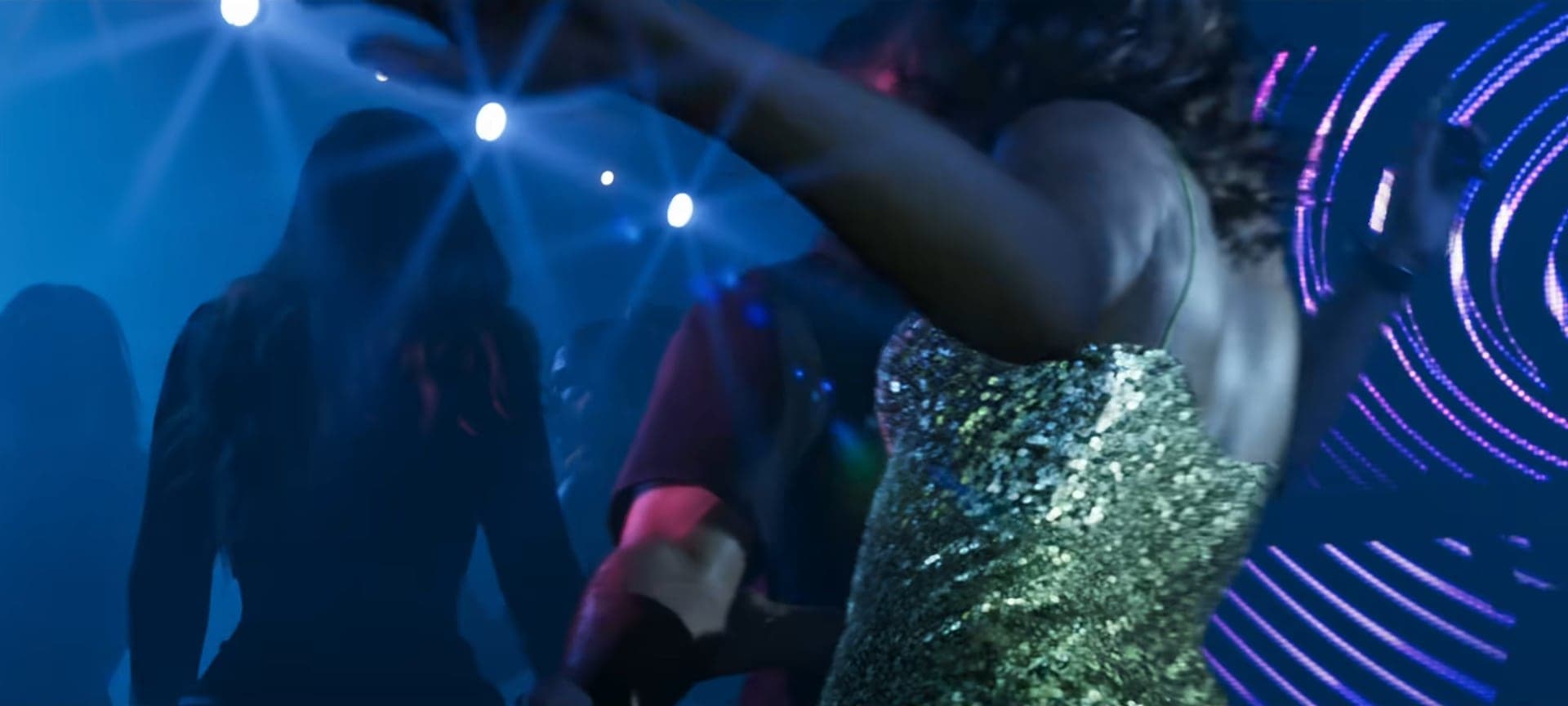 A woman in a sequined dress on a dance floor with neon rings and spotlights