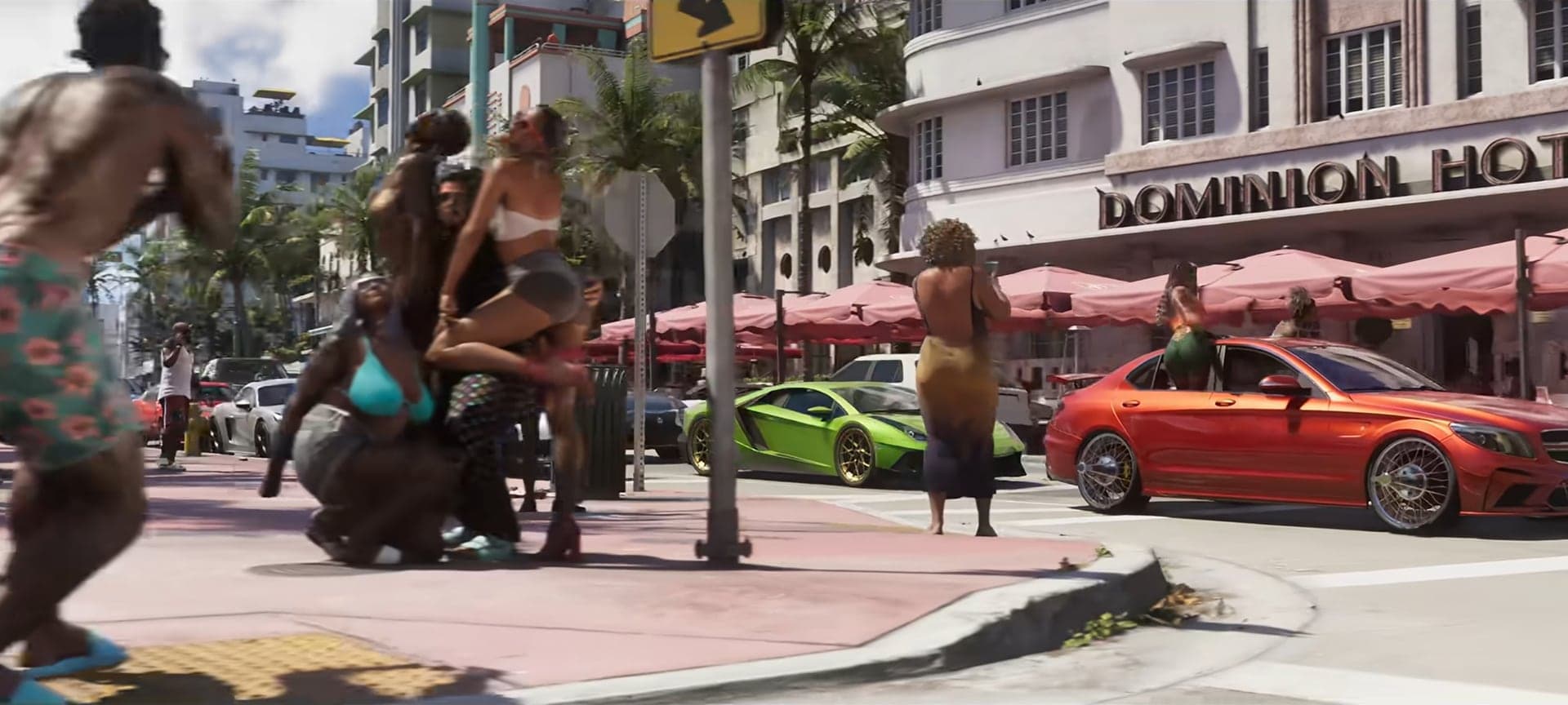 People on a sunny sidewalk outside the Dominion Hotel, sports cars by the curb